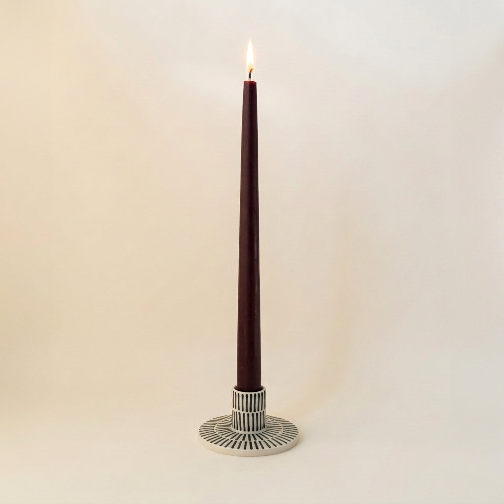 Handgjord ljusstake i stengods med smala handmålade svarta ränder och transparent glasyr, med ett tänt vinrött kronljus.