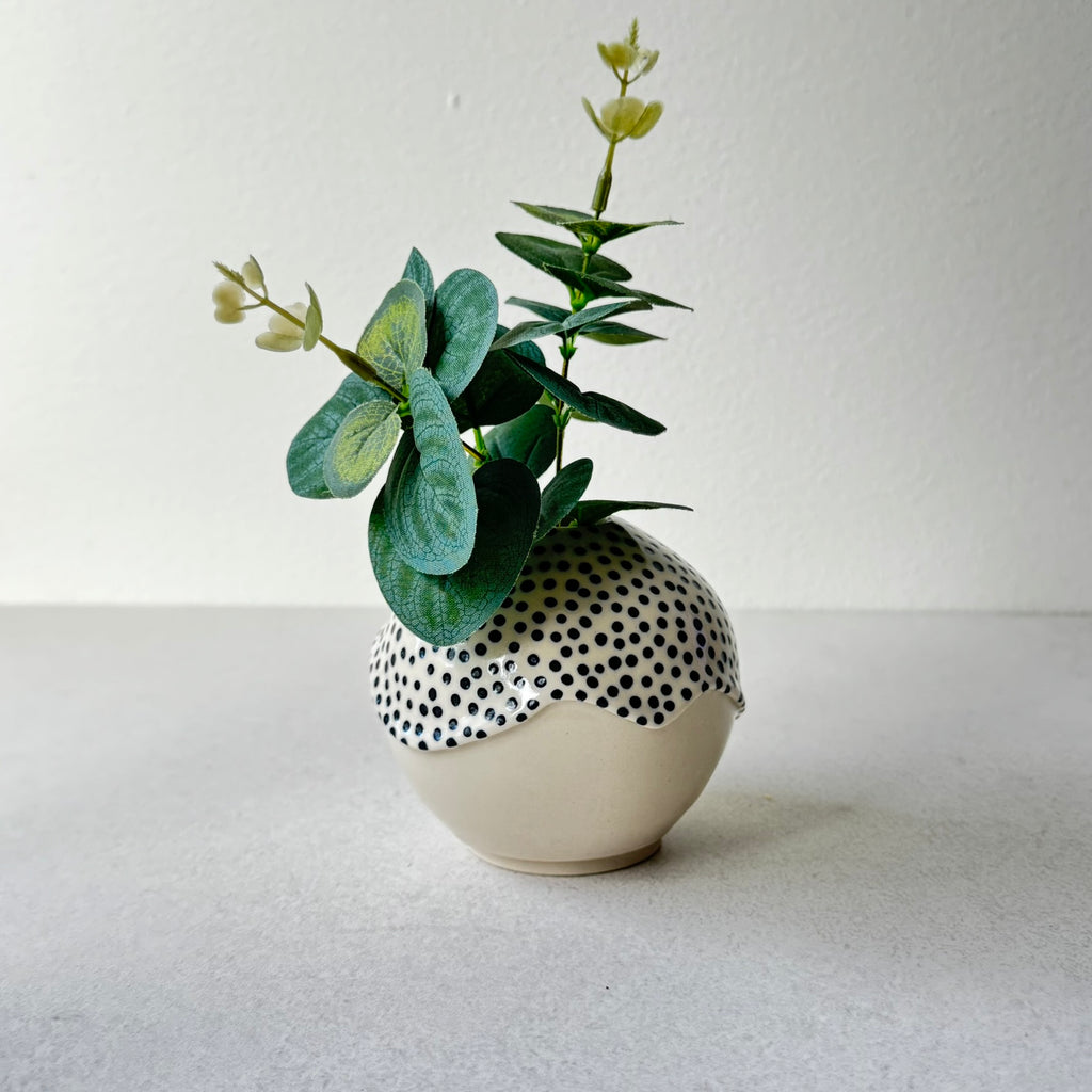 Handgjord rund vas i stengods med handmålade svarta prickar och transparent glasyr med rinnande kant, dekorerad med grönska